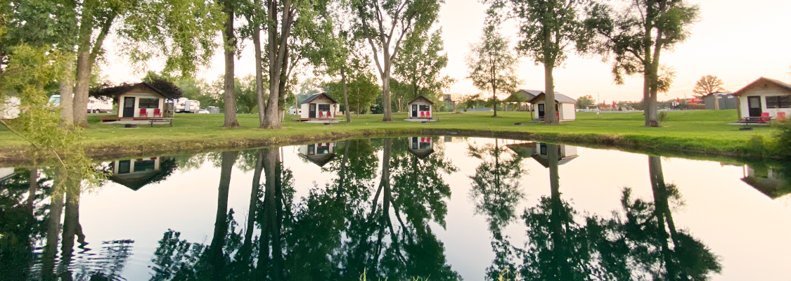 5 cabins around the pond with trees and reflection off the water