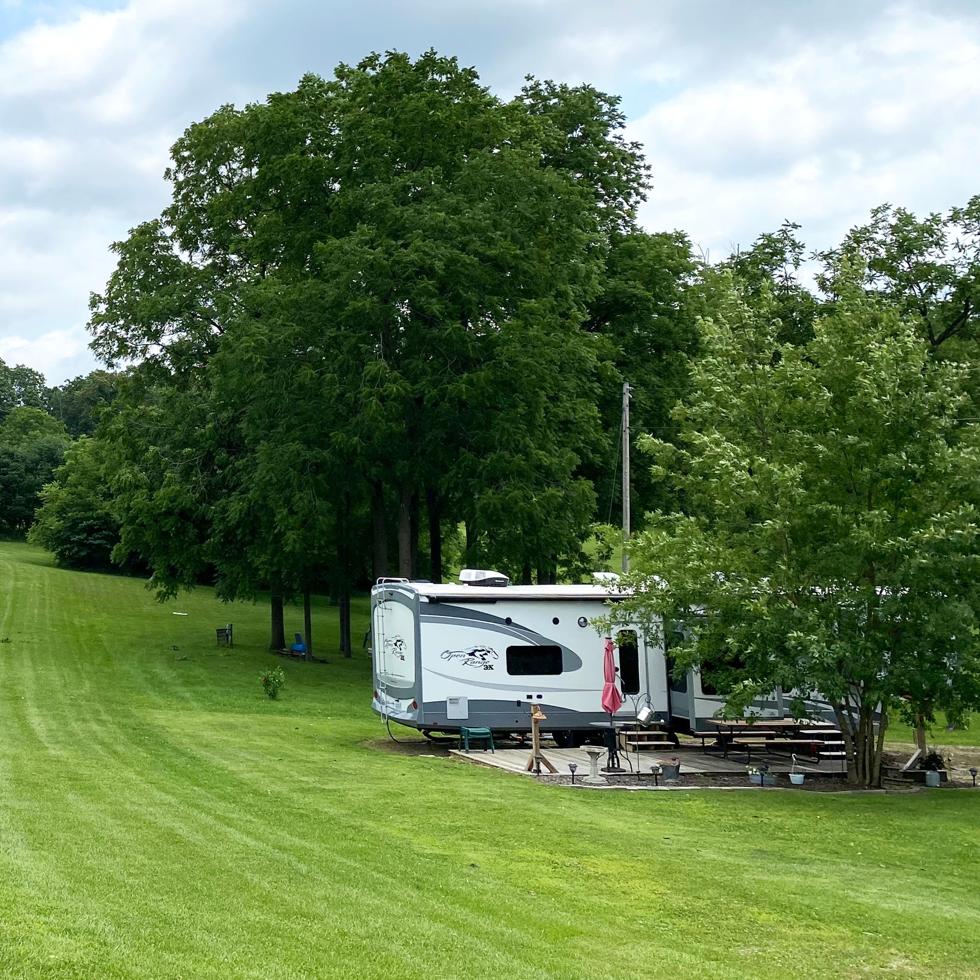 rv with a deck set up under mature trees.