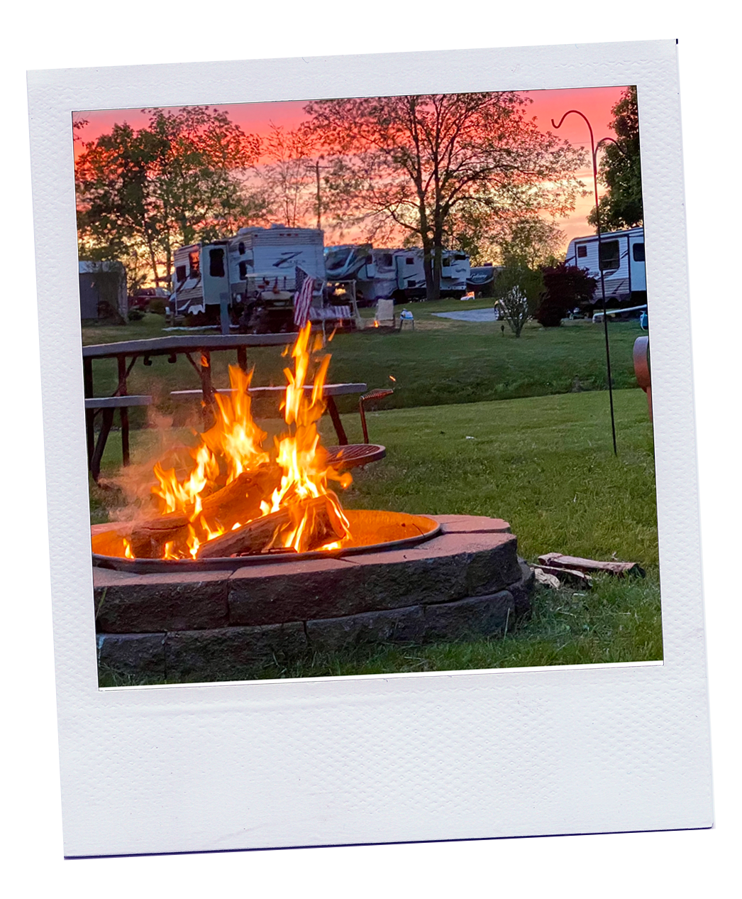 poleriod picture of a campfire with campers and a sunset in the background